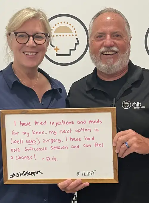 Two people pose in front of a Shift Health Center backdrop while holding a whiteboard testimonial. The message describes trying injections and medications for knee pain, facing possible surgery, and noticing positive changes after one SoftWave session.